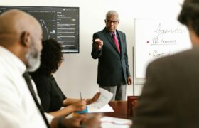 Senior executive conducting a business meeting with colleagues, discussing agenda on a whiteboard.