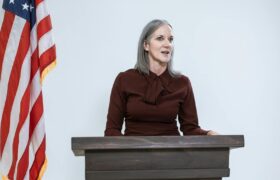 Confident woman delivering speech in front of an American flag, embodying leadership and empowerment.