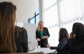 A business team in a modern office engaged in a presentation led by a woman, fostering teamwork and collaboration.
