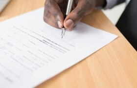 A hand holding a pen signing a document close-up on a desk, symbolizing agreement or contract finalization.