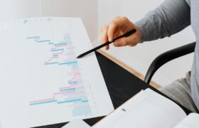 Close-up of a person analyzing a colorful graph chart with a pen in a modern office setting.
